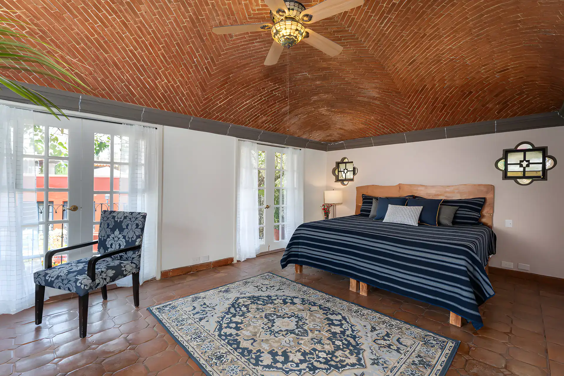 Villa Escondida, bedroom with a navy striped bed, patterned armchair and French doors under a brick ceiling, San Miguel de Allende