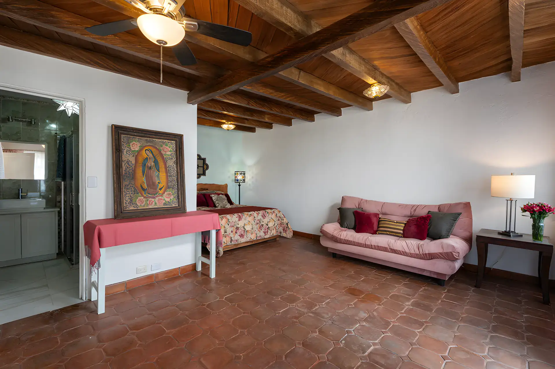 Villa Escondida, bedroom with a wood-beam ceiling, a painted Virgin artwork and a pink sofa, San Miguel de Allende