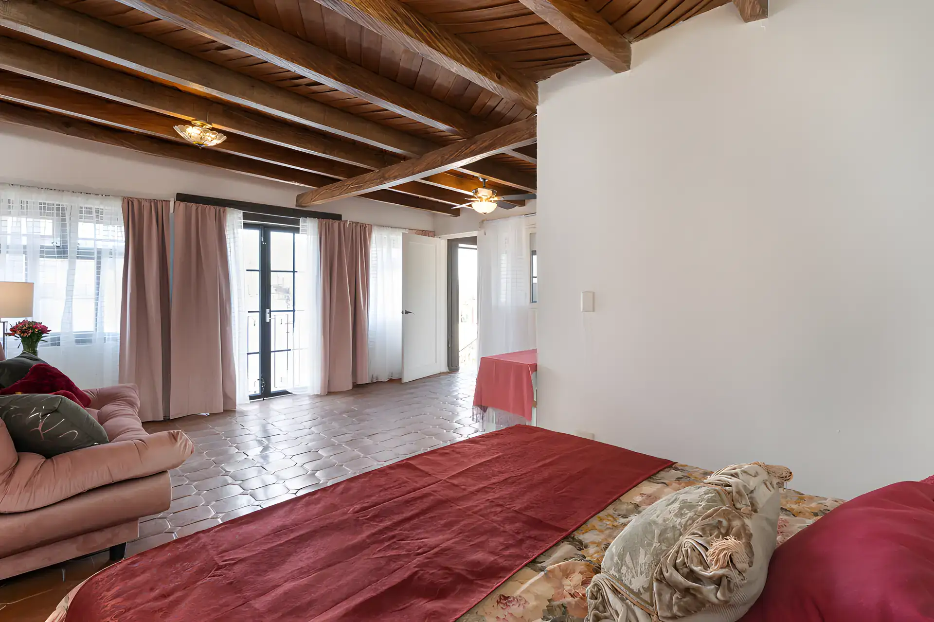 Villa Escondida, bedroom suite with a red bedspread, wood-beam ceiling and tall windows with curtains, San Miguel de Allende