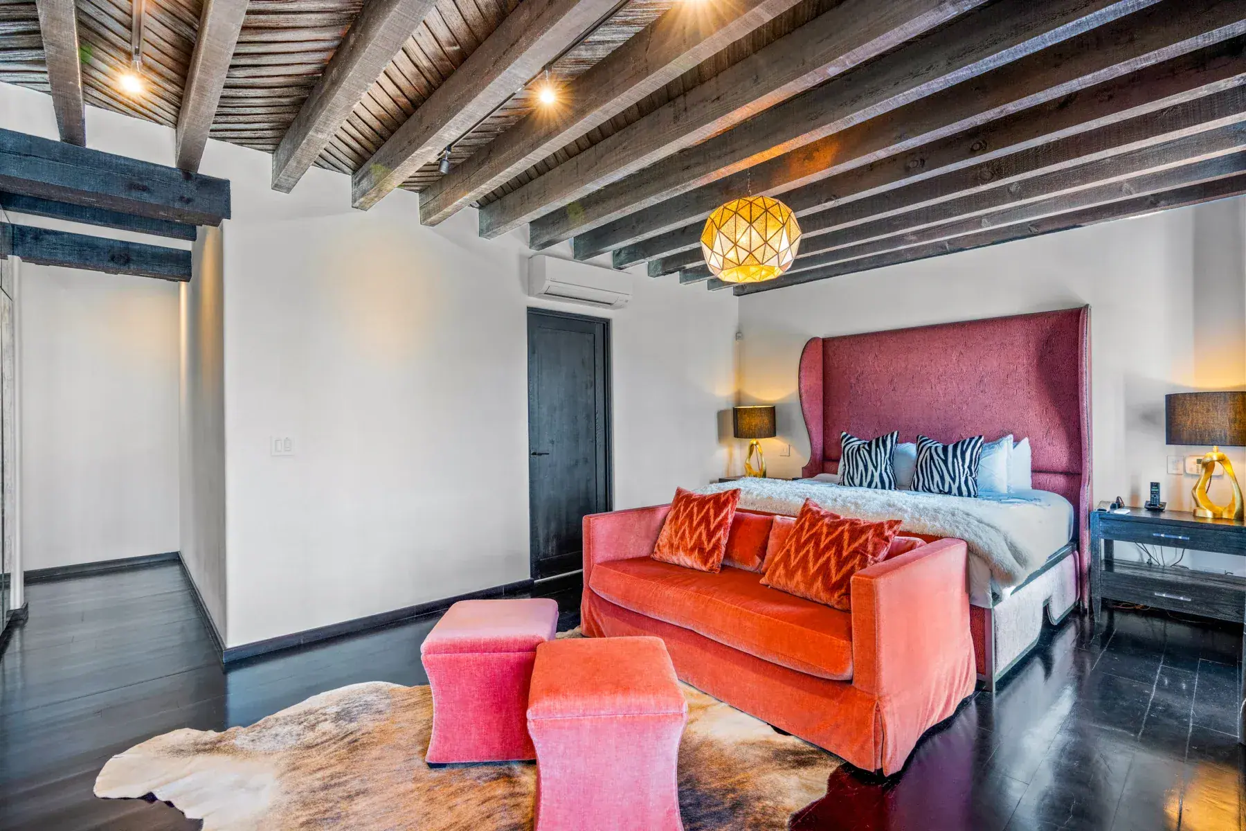 Villa Garita, primary bedroom with a coral sofa, tall headboard and a wood beam ceiling, San Miguel de Allende