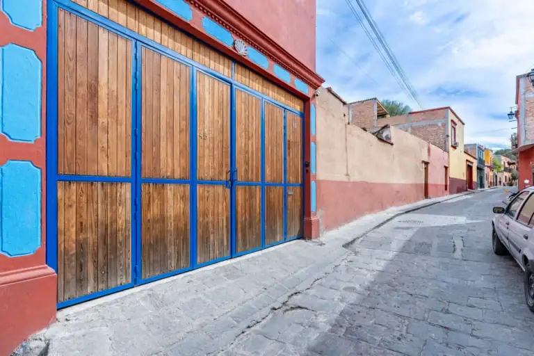 Villa Guacamayas, blue-framed wooden garage doors on a red facade along a cobblestone street, San Miguel de Allende
