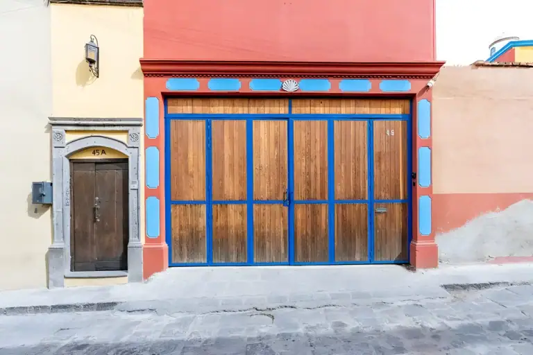Villa Guacamayas, street entrance with a wooden garage door and an arched wooden pedestrian door, San Miguel de Allende