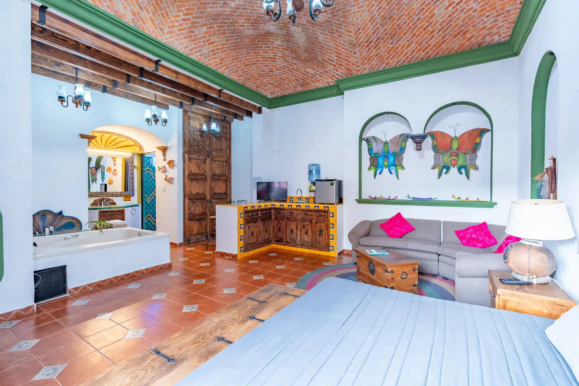 Villa Guacamayas, studio suite with a tiled kitchenette, butterfly wall art, brick vaulted ceiling and a gray sofa, San Miguel de Allende