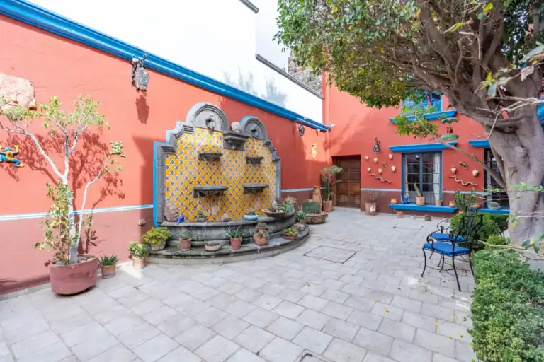 Villa Guacamayas, courtyard with a tiled wall fountain, potted plants and a red wall with blue trim, San Miguel de Allende