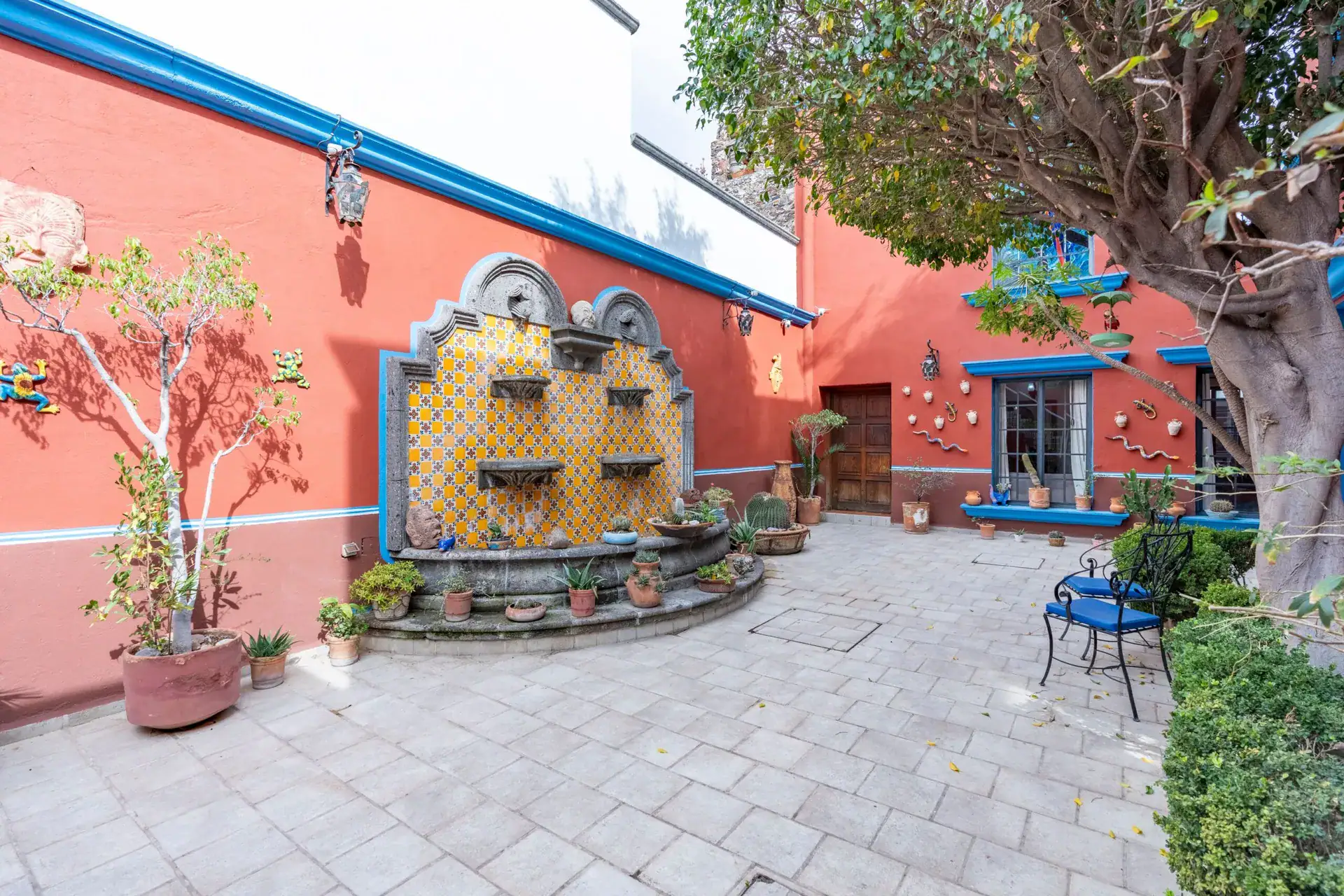 Villa Guacamayas, courtyard with a tiled wall fountain, potted plants and a red wall with blue trim, San Miguel de Allende