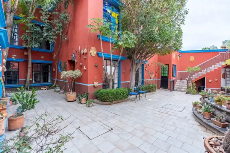 Villa Guacamayas, red-walled courtyard with trees, stone paving and an exterior staircase, San Miguel de Allende