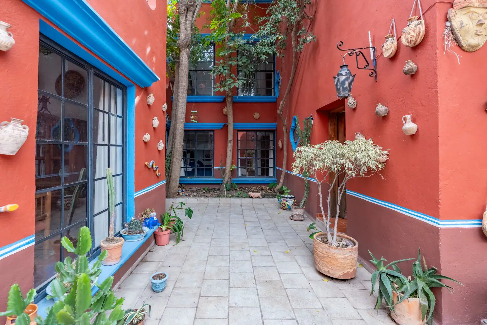 Villa Guacamayas, courtyard corner with large glass doors, potted plants and wall-mounted pottery, San Miguel de Allende