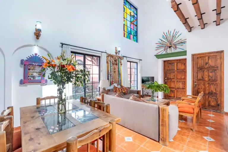 Villa Guacamayas, living room with a gray sofa, wood dining table, stained glass window and beamed ceiling, San Miguel de Allende