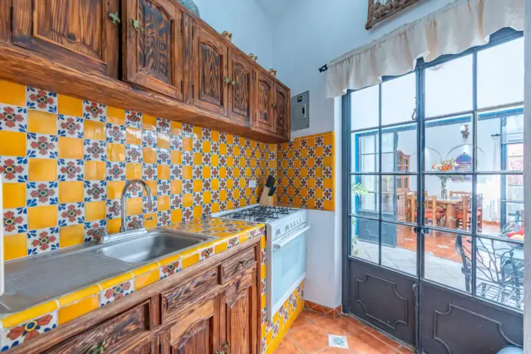 Villa Guacamayas, kitchen with yellow and blue Talavera tile, carved wood cabinets and glass doors to the courtyard, San Miguel de Allende
