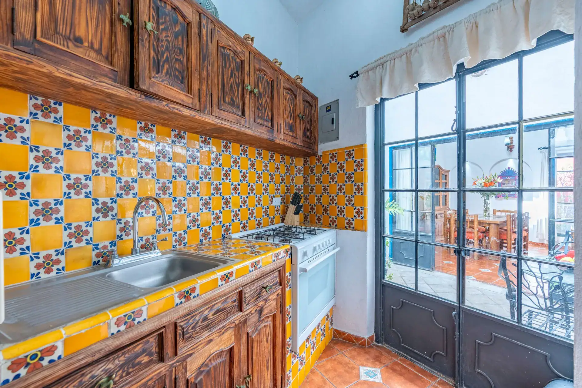 Villa Guacamayas, kitchen with yellow and blue Talavera tile, carved wood cabinets and glass doors to the courtyard, San Miguel de Allende