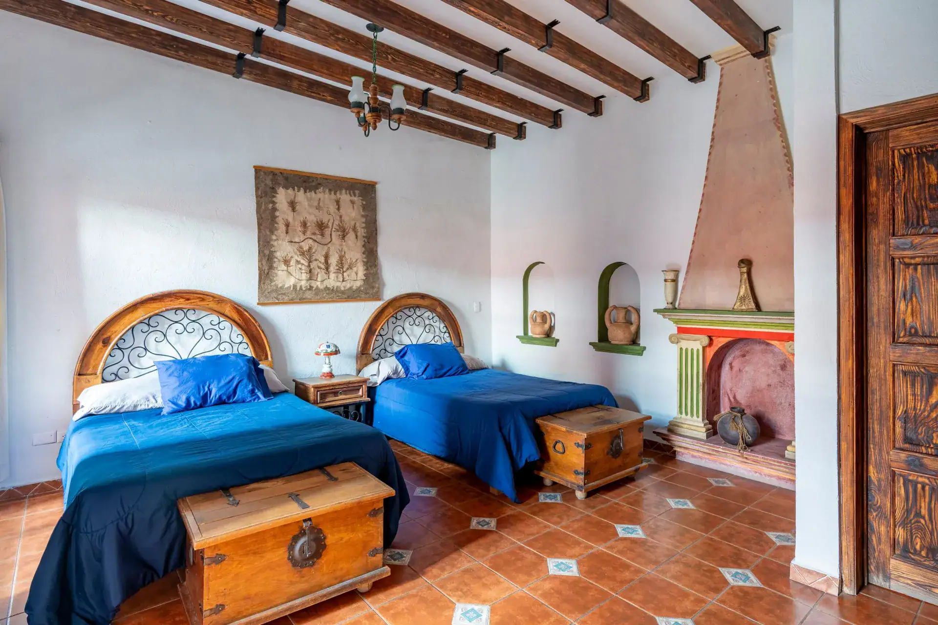 Villa Guacamayas, bedroom with two twin beds, wrought-iron headboards, a chest and a corner fireplace, San Miguel de Allende