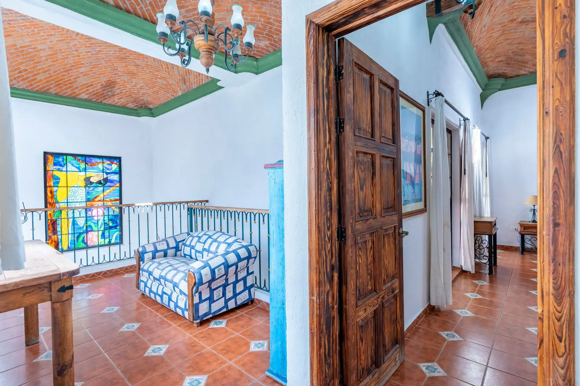 Villa Guacamayas, loft sitting area with a stained glass window and an upholstered chair beside a carved wood door, San Miguel de Allende