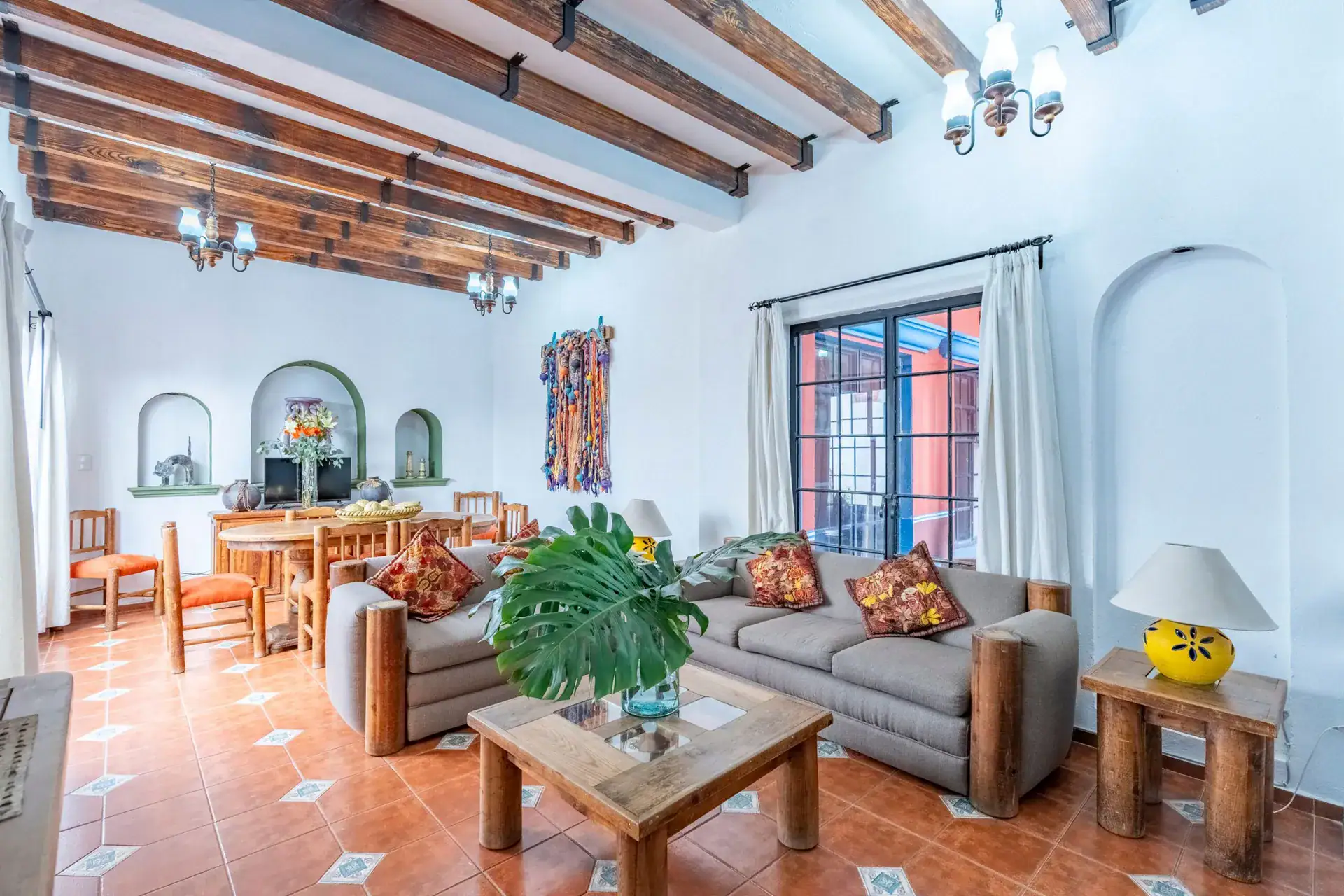 Villa Guacamayas, living and dining area with a gray sofa, beamed ceiling and an arched niche, San Miguel de Allende