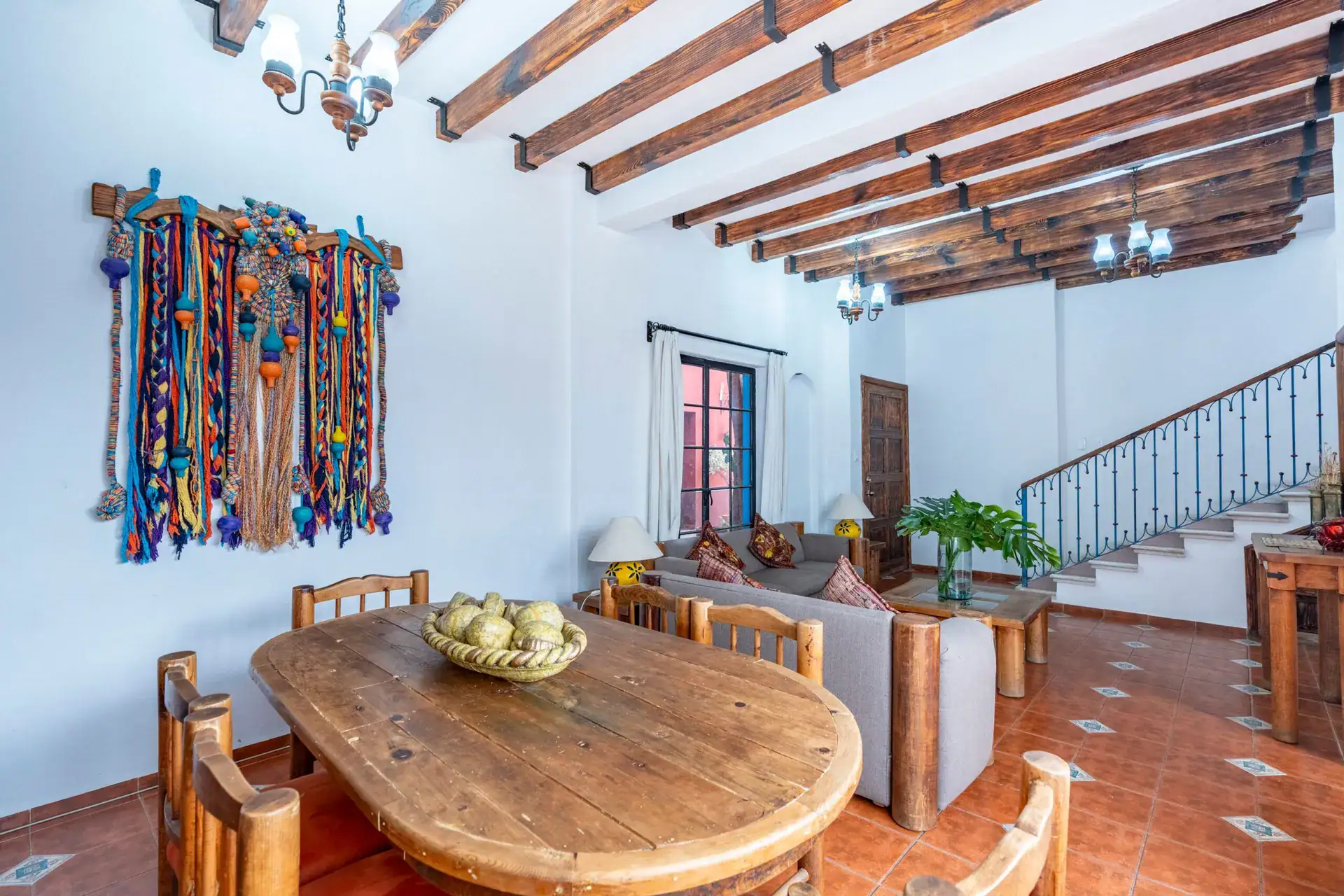Villa Guacamayas, dining table and sofa with a woven wall hanging under a beamed ceiling, San Miguel de Allende