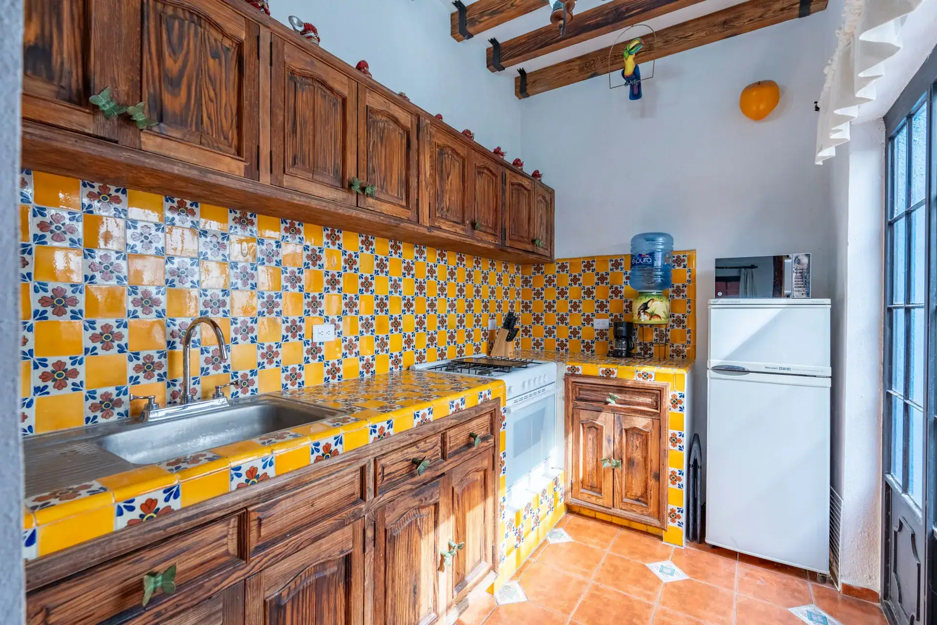 Villa Guacamayas, kitchen with yellow and blue tile, carved wood cabinets and a white refrigerator, San Miguel de Allende