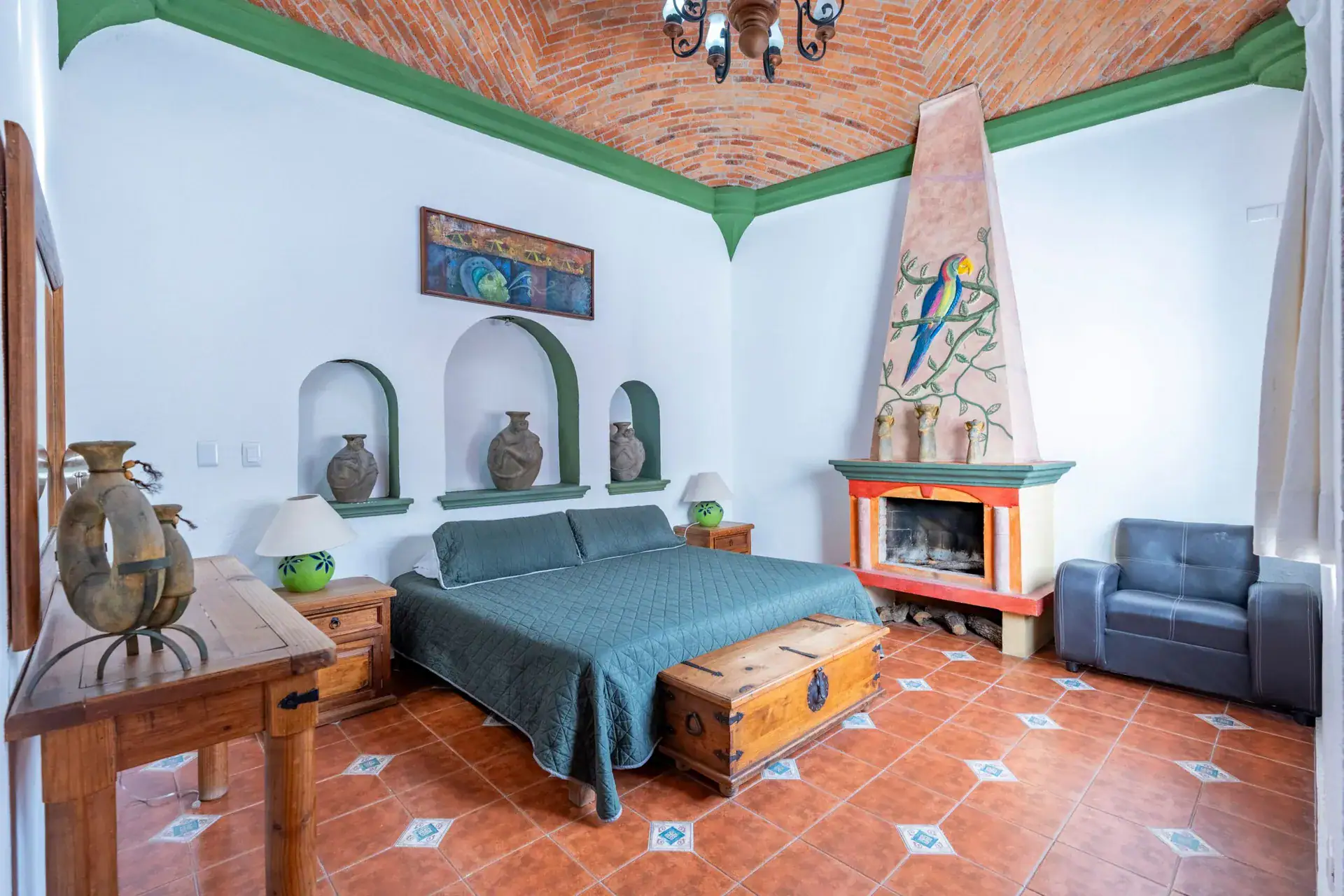 Villa Guacamayas, bedroom with a green bedspread, painted parrot fireplace and brick vaulted ceiling, San Miguel de Allende