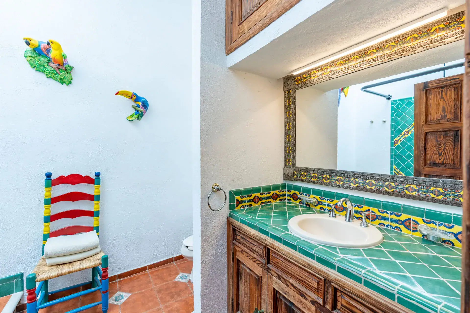 Villa Guacamayas, bathroom with a green tile vanity, ornate mirror and a colorful wooden chair, San Miguel de Allende