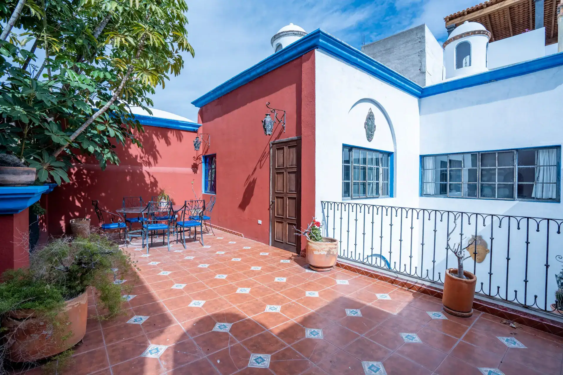 Villa Guacamayas, rooftop terrace with a dining set, red walls and a blue-trimmed white building, San Miguel de Allende