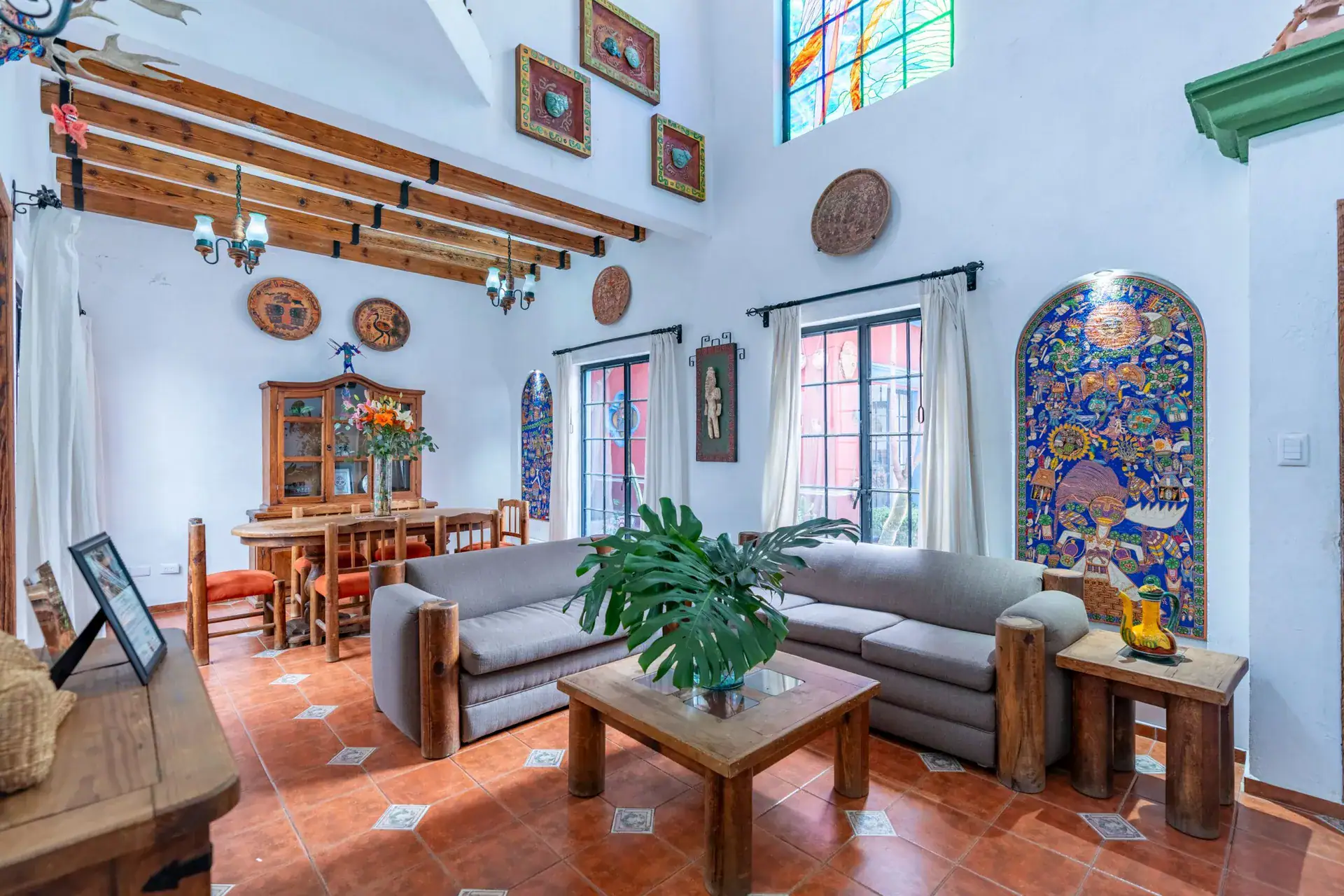 Villa Guacamayas, living and dining room with gray sofas, a wood table and a large painted tile mural, San Miguel de Allende