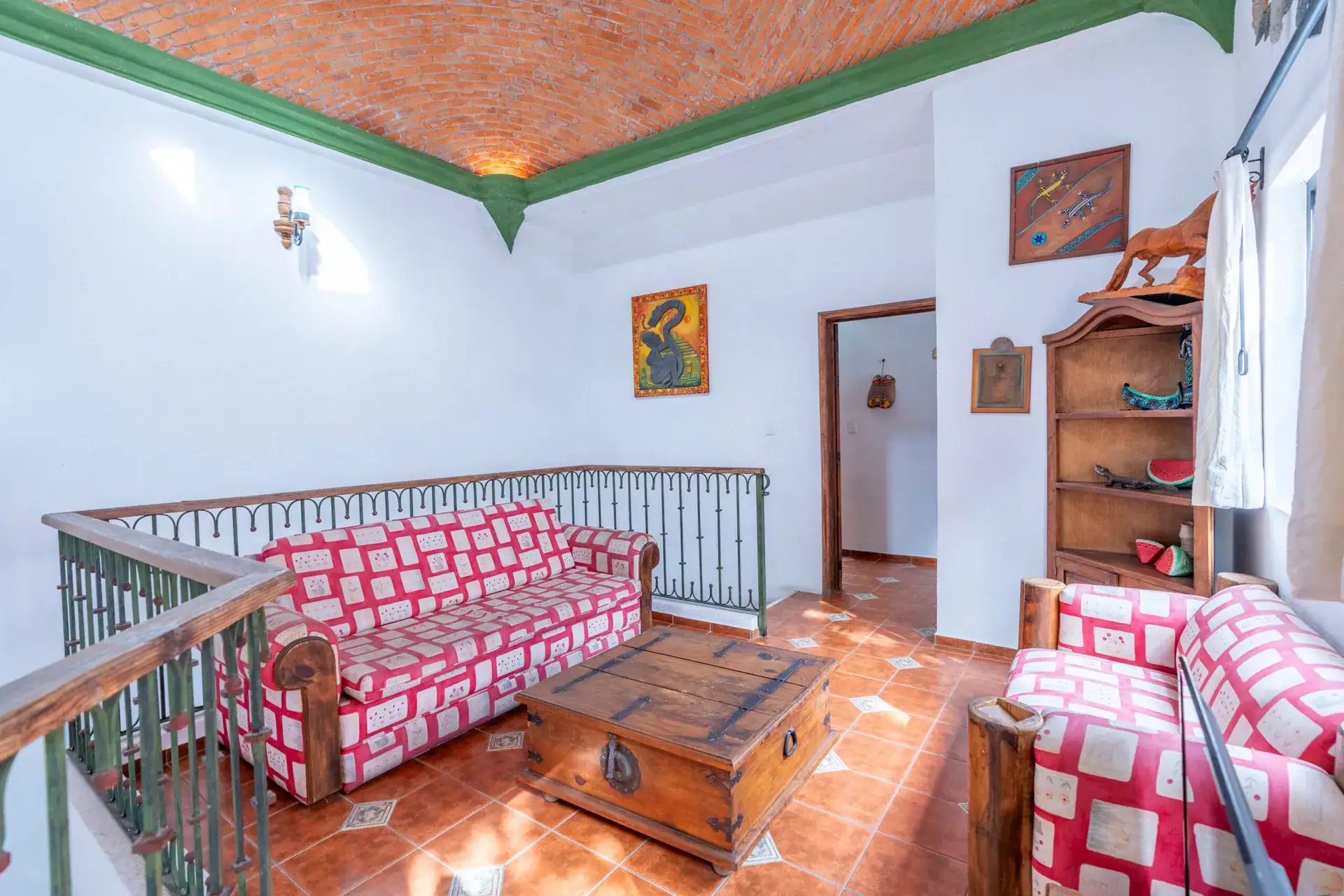 Villa Guacamayas, upstairs sitting area with a red and white patterned sofa, chest table and an iron railing, San Miguel de Allende