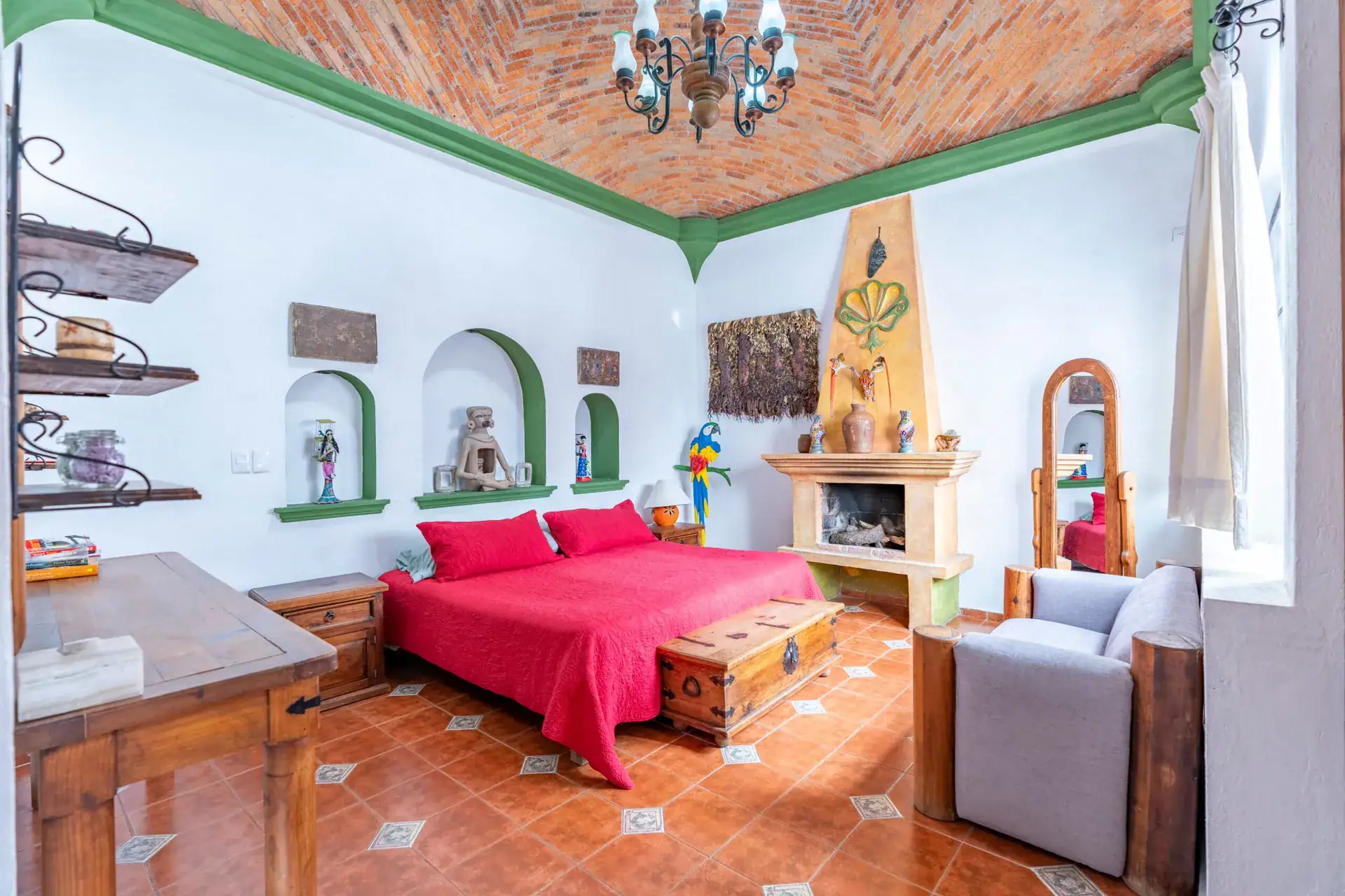 Villa Guacamayas, bedroom with a red bedspread, painted fireplace and brick vaulted ceiling, San Miguel de Allende