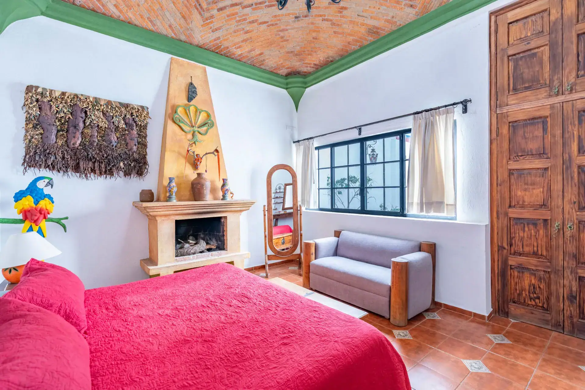 Villa Guacamayas, bedroom with a red bed, fireplace, armchair and a large carved door, San Miguel de Allende