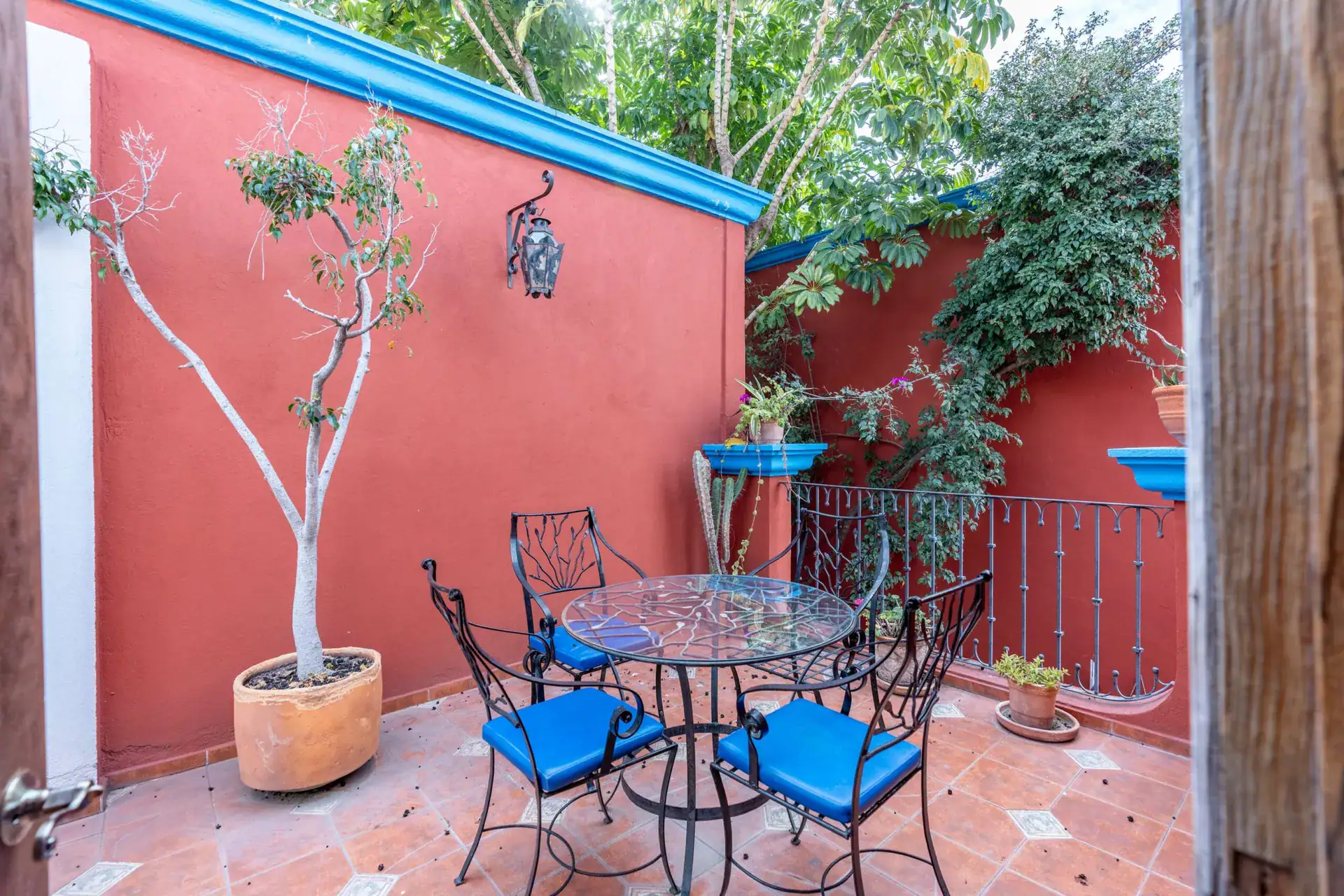 Villa Guacamayas, small terrace with a bistro table and blue chairs beside a red wall and a potted tree, San Miguel de Allende