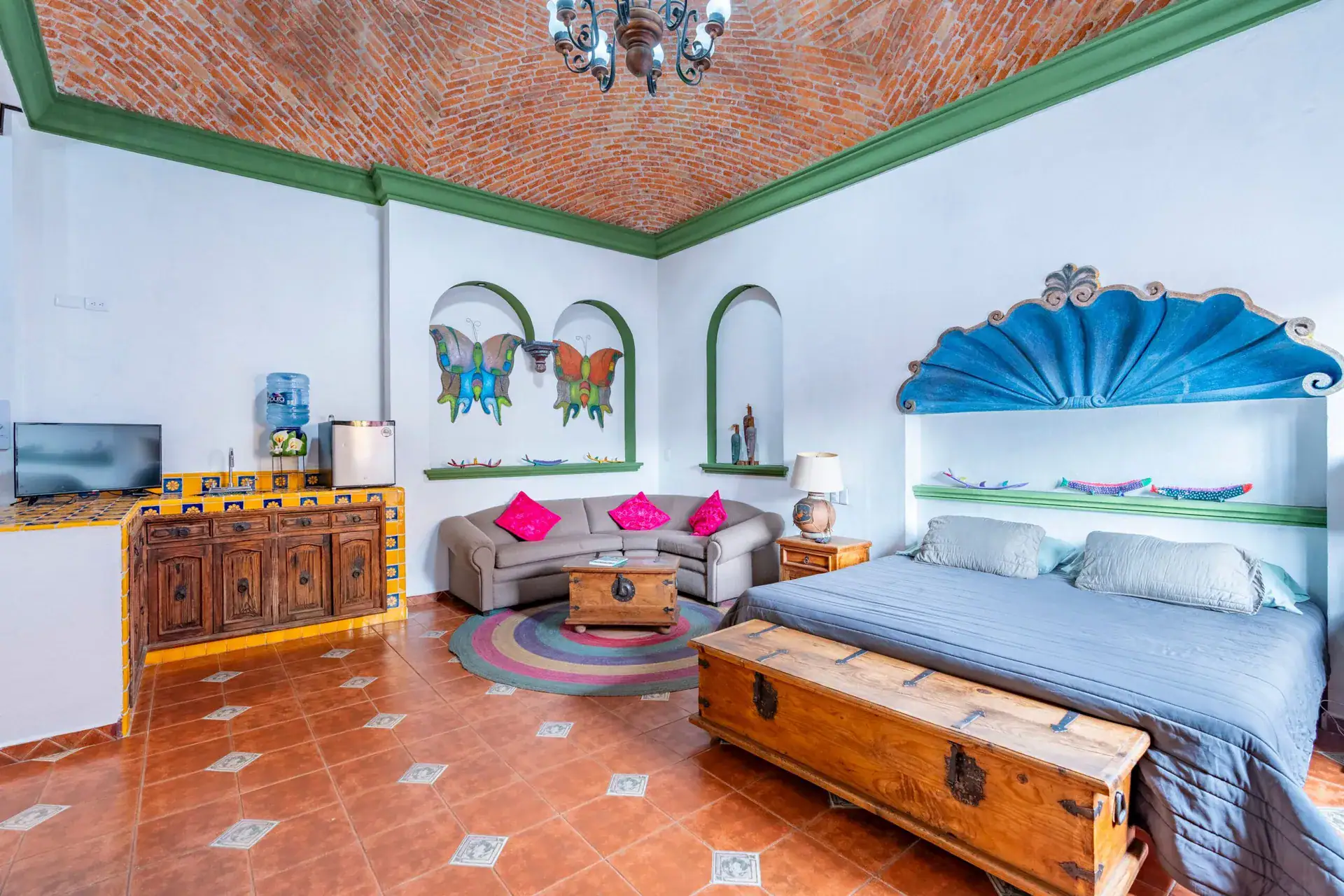 Villa Guacamayas, suite with a king bed under a blue shell-shaped headboard, a tiled kitchenette and a brick vaulted ceiling, San Miguel de Allende