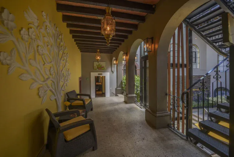 Villa Limón, corridor with a yellow wall, a carved tree relief and wood beams, San Miguel de Allende