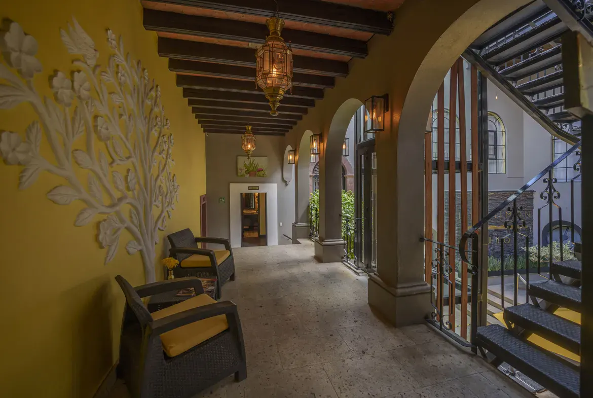 Villa Limón, corridor with a yellow wall, a carved tree relief and wood beams, San Miguel de Allende