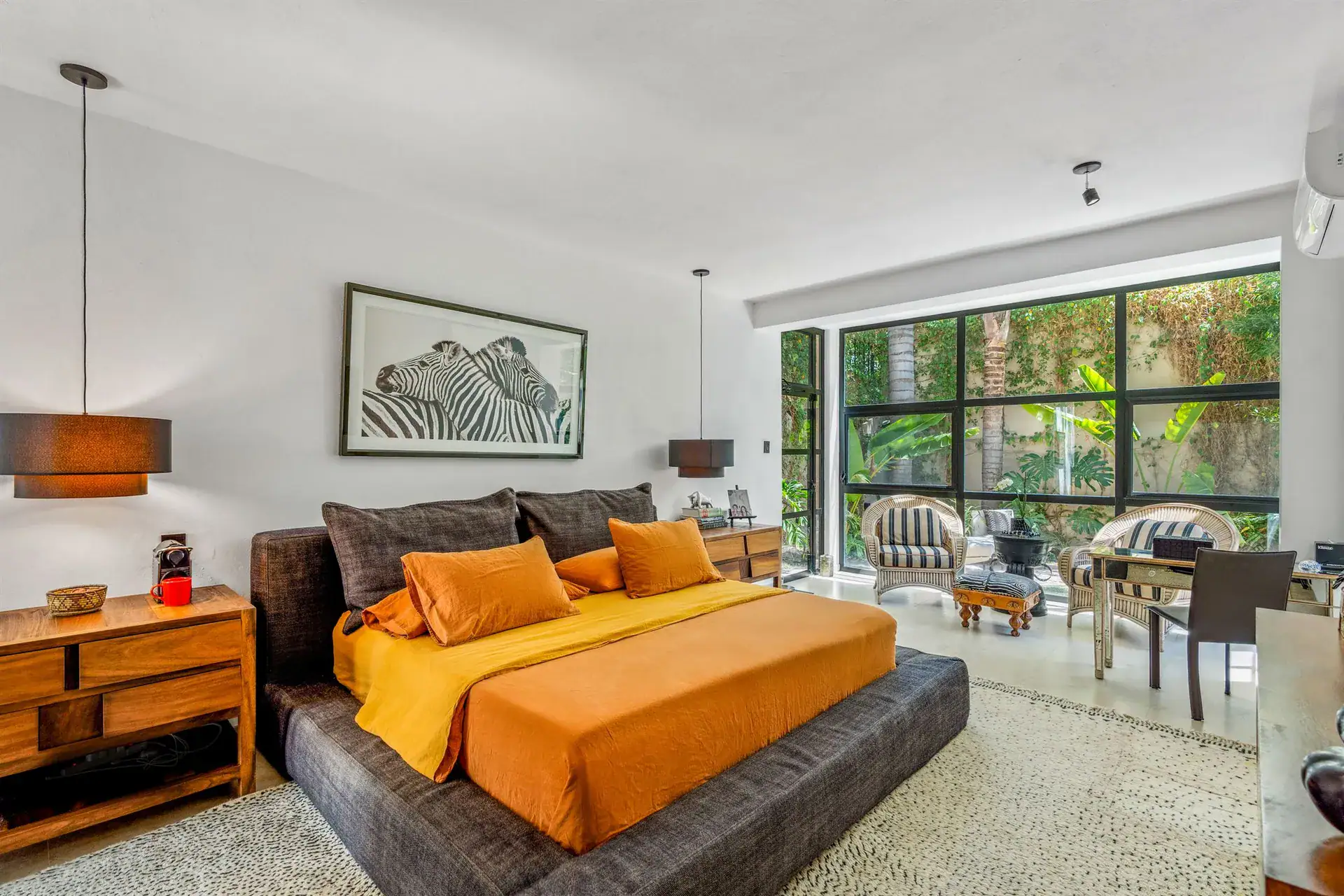 Villa Pacifica, bedroom with a low platform bed, an orange bedspread and a wall of garden windows, San Miguel de Allende