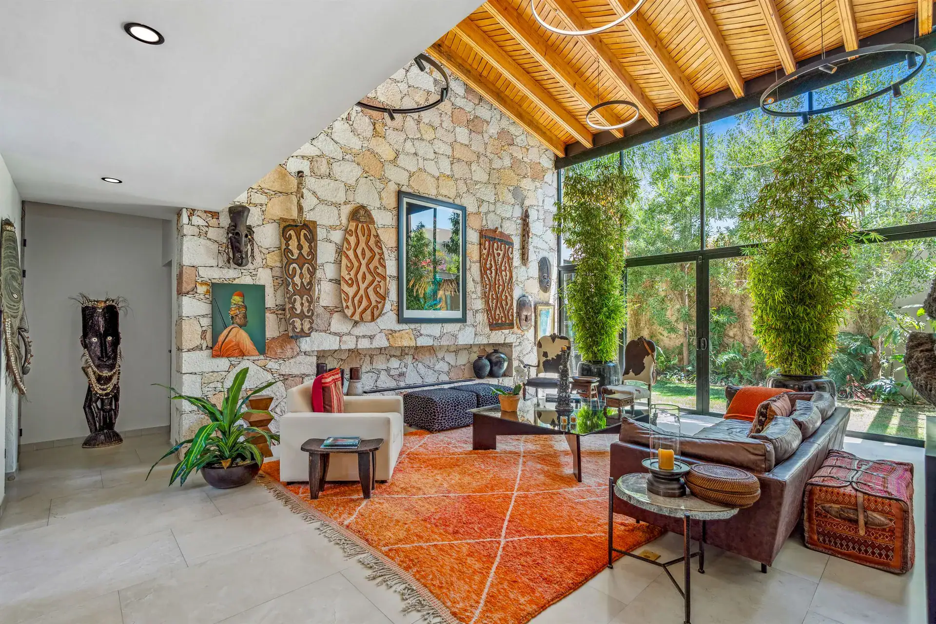 Villa Pacifica, living room with a stone feature wall, a tall wood figure, orange rugs and sofas under a wood-slat ceiling, San Miguel de Allende