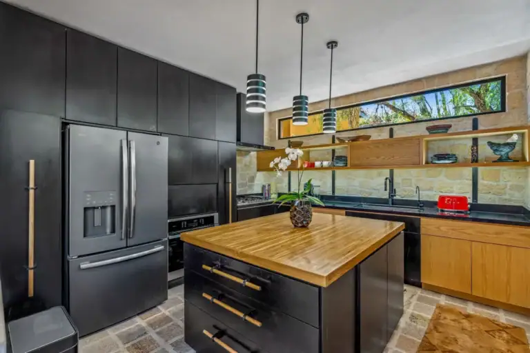 Villa Pacifica, kitchen with black cabinets, a butcher-block island, pendant lights and a stone wall, San Miguel de Allende