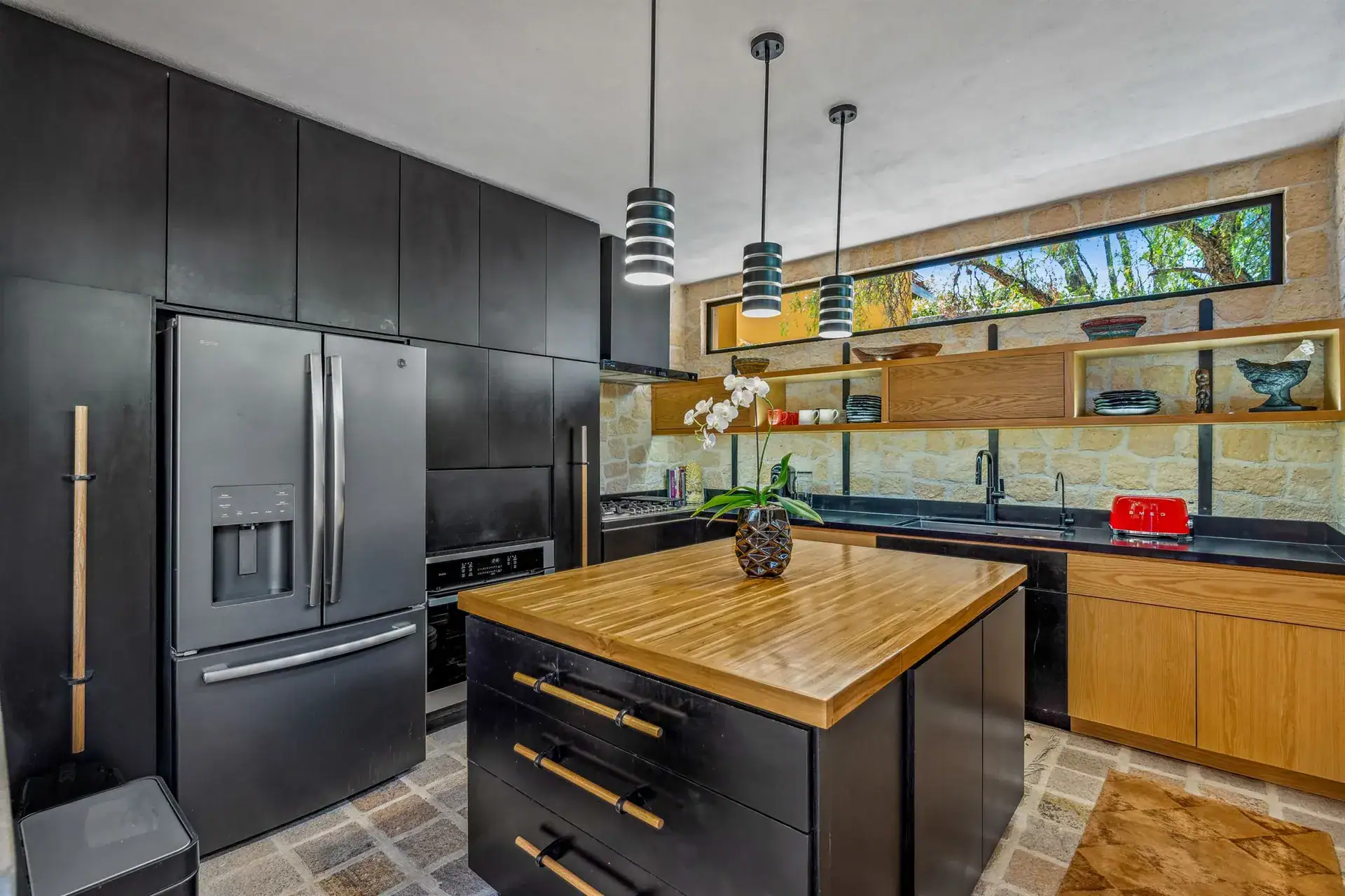 Villa Pacifica, kitchen with black cabinets, a butcher-block island, pendant lights and a stone wall, San Miguel de Allende