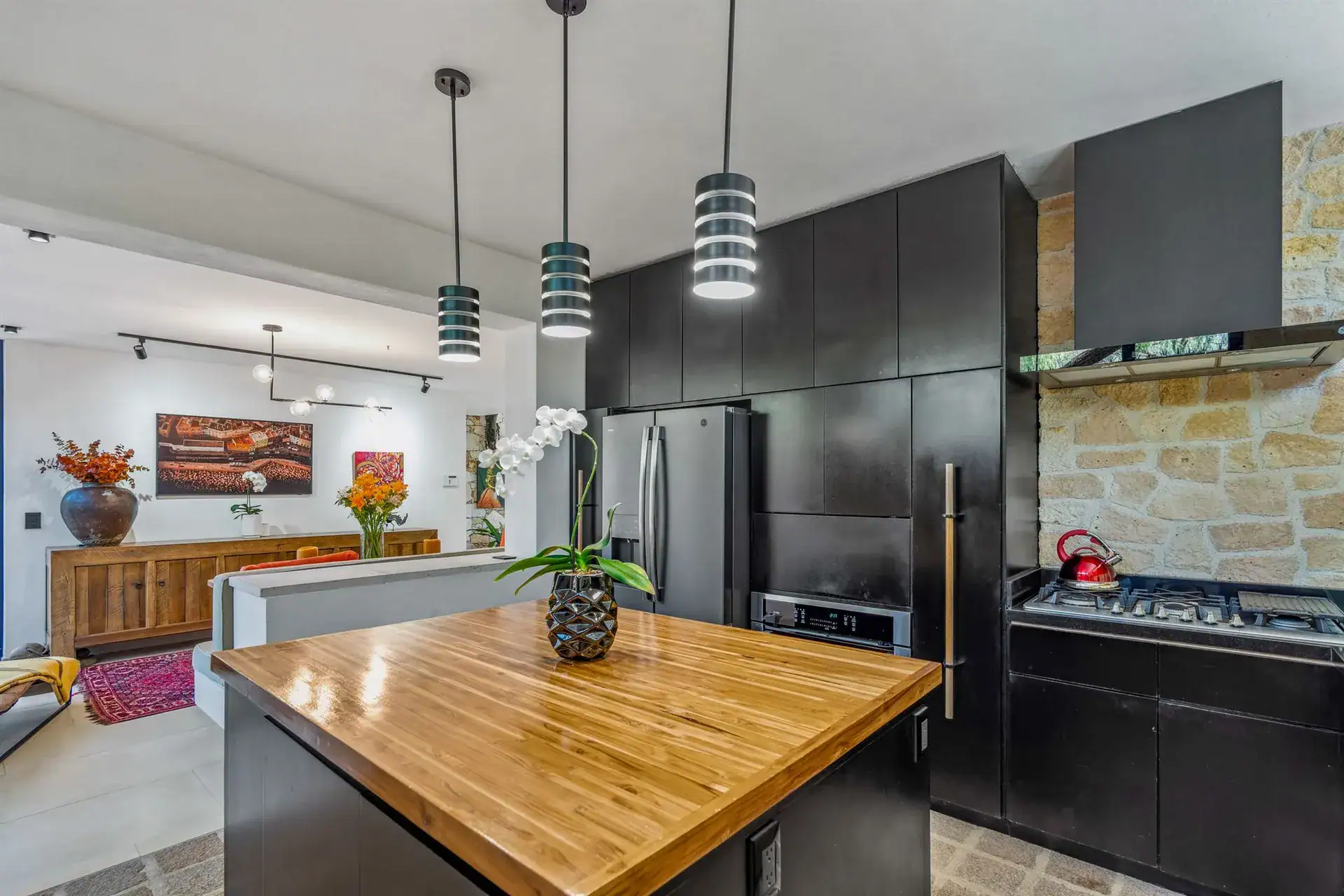 Villa Pacifica, kitchen with a black range hood, a gas cooktop and a wood island under striped pendant lights, San Miguel de Allende