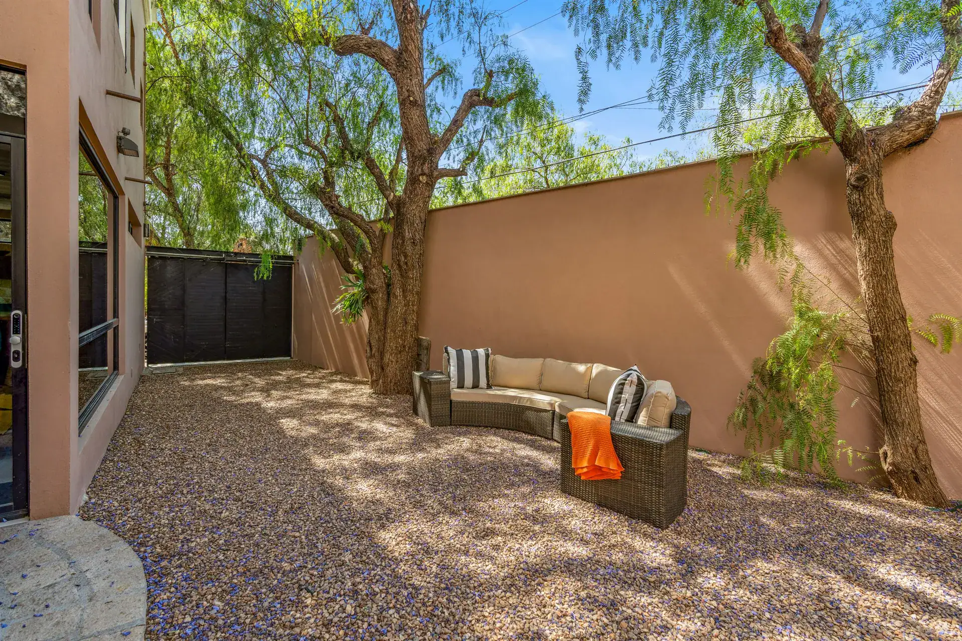 Villa Pacifica, gravel patio with a curved outdoor sofa under pepper trees and a pink wall, San Miguel de Allende