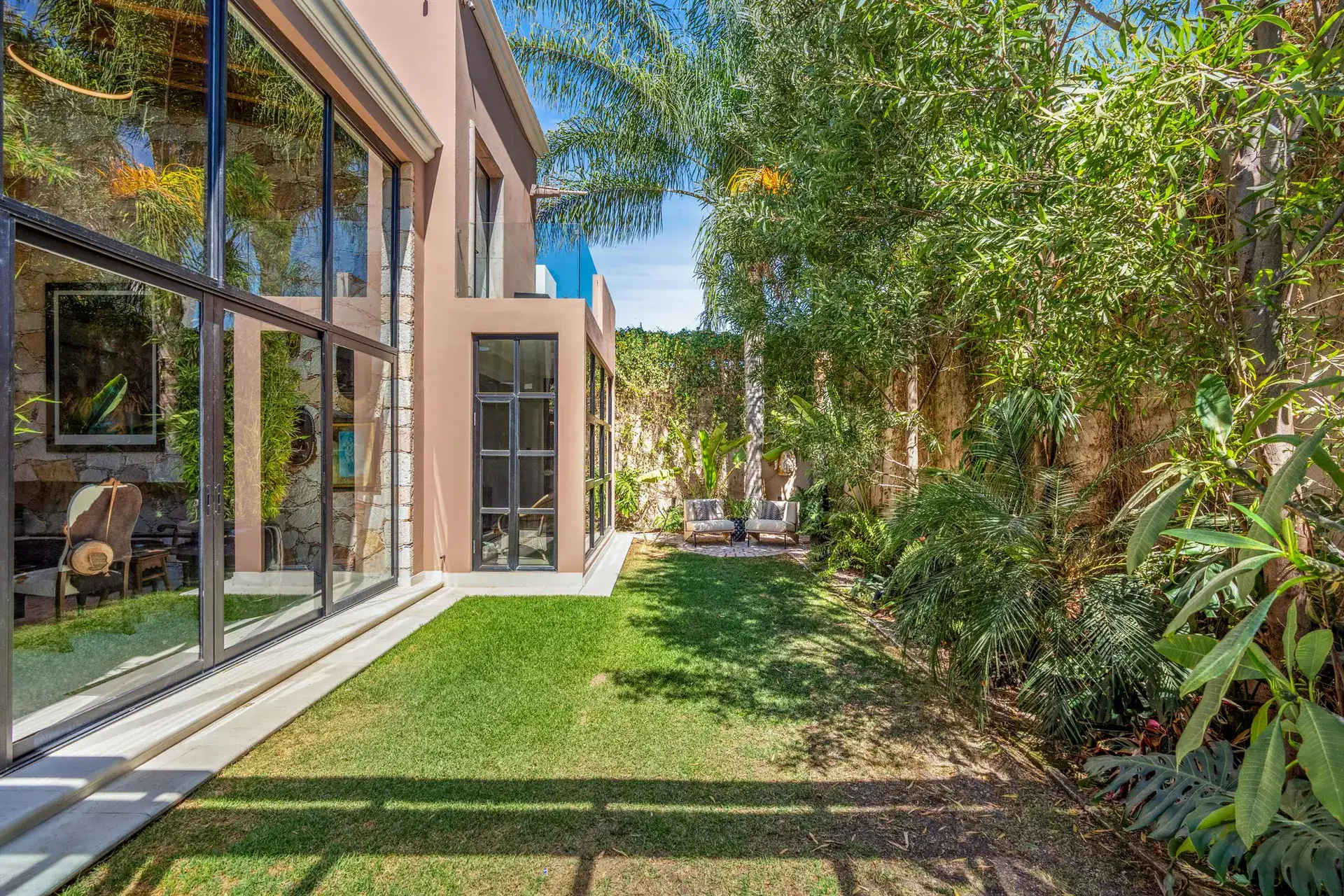 Villa Pacifica, back lawn with palm trees and the glass-walled two-story house, San Miguel de Allende