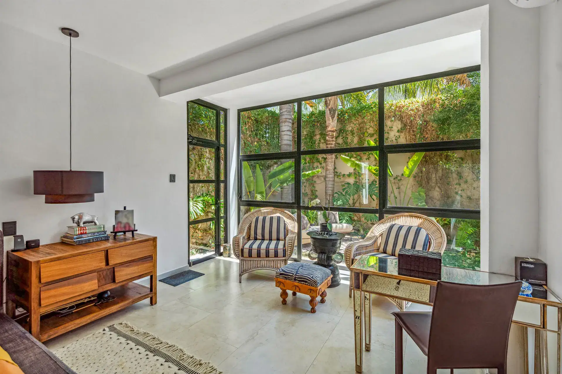 Villa Pacifica, sunroom with wicker armchairs, a wood console and a wall of glass windows, San Miguel de Allende