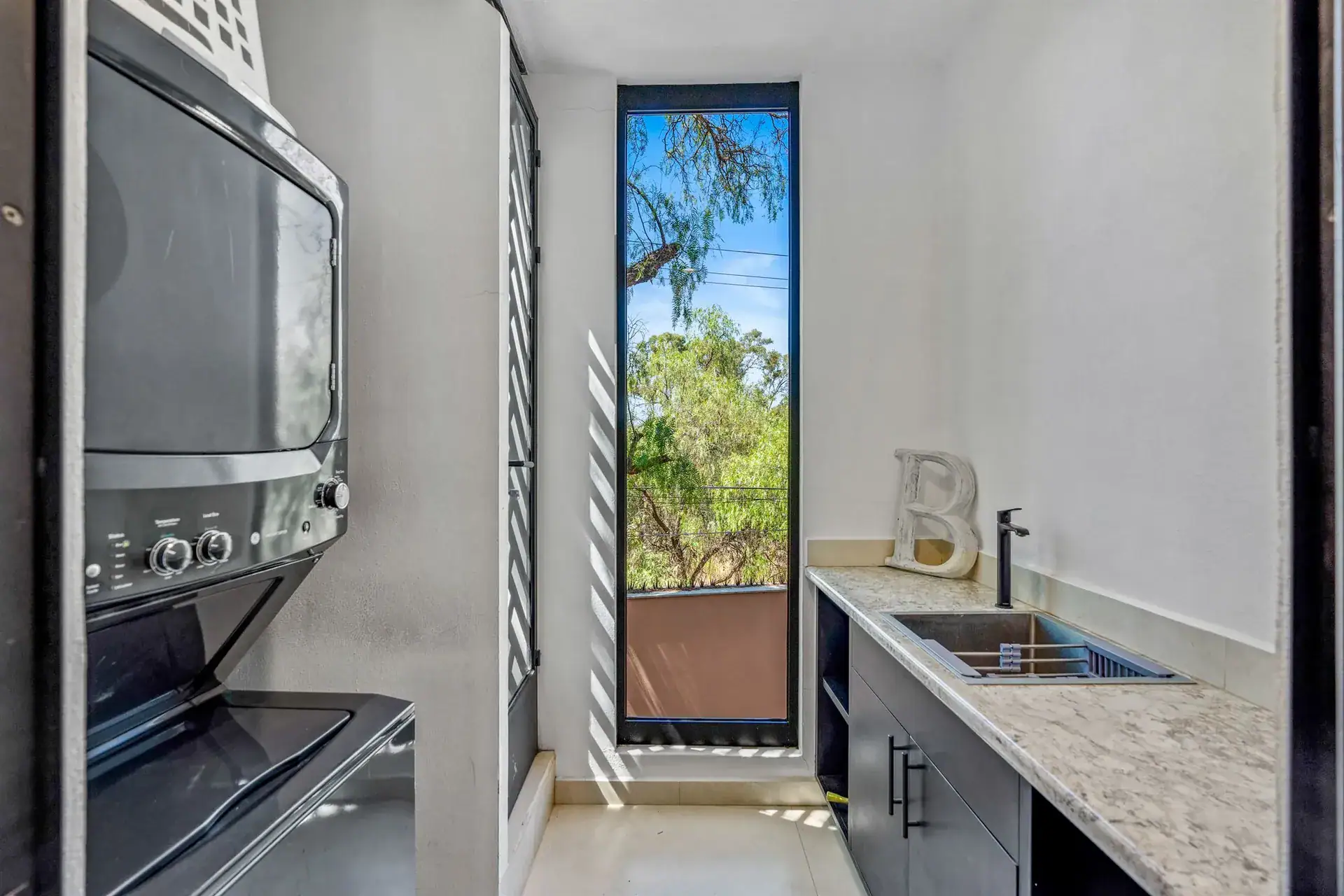 Villa Pacifica, laundry nook with a stacked washer and dryer, a sink and a tall narrow window, San Miguel de Allende