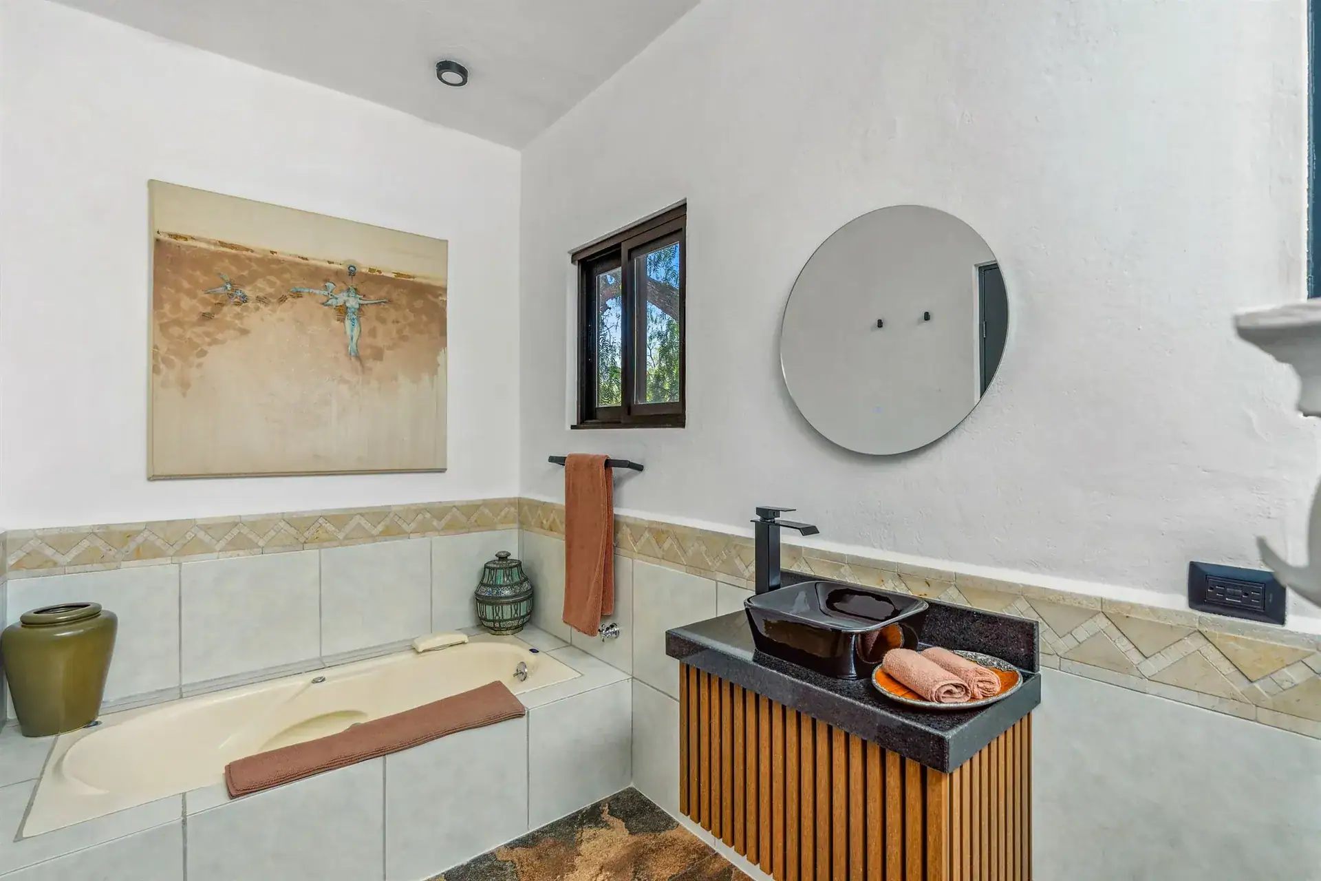 Villa Pacifica, bathroom with a tiled tub, a black sink on a slatted vanity and a round mirror, San Miguel de Allende