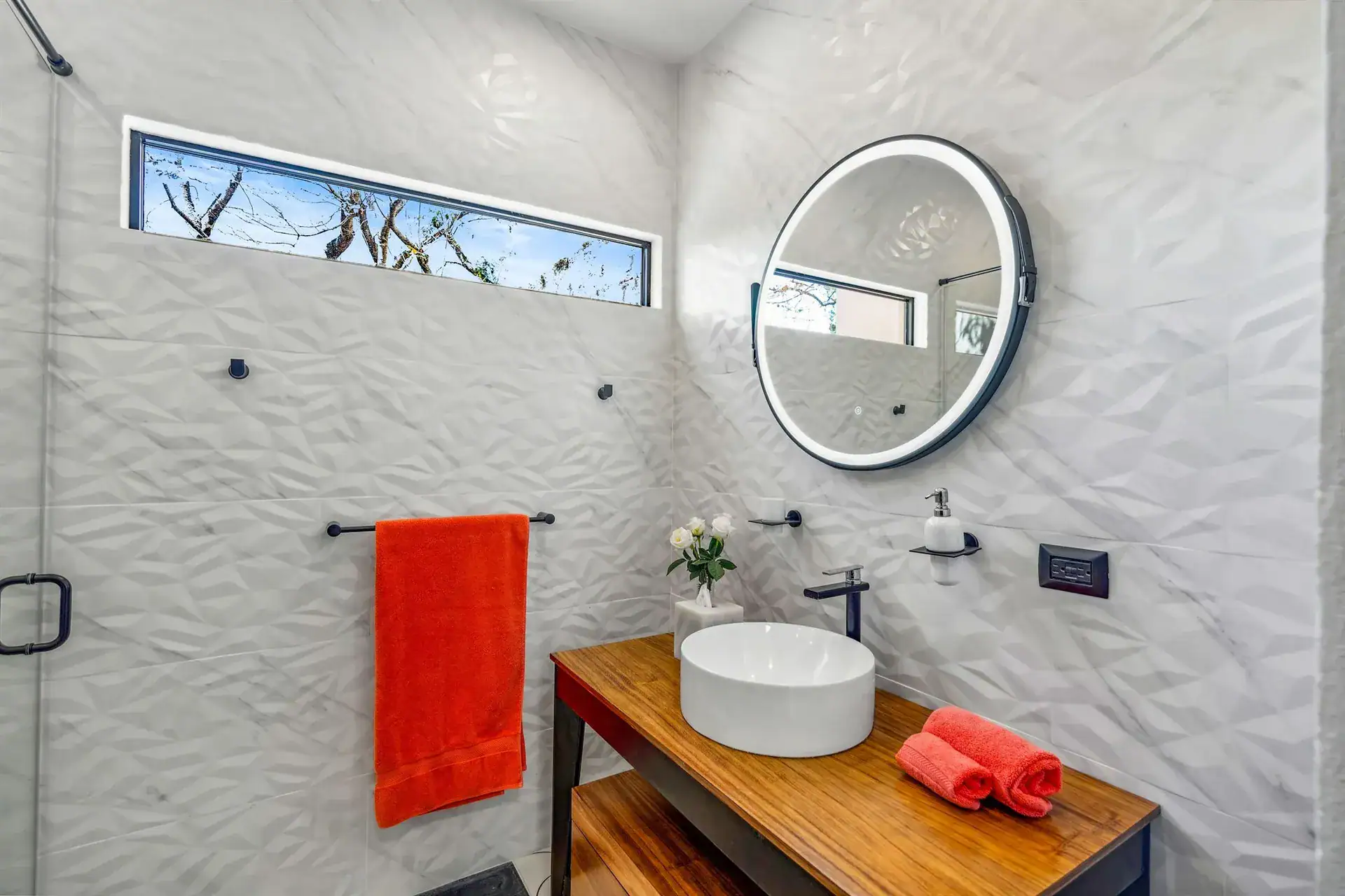 Villa Pacifica, bathroom with a textured white tile shower, a wood vanity and a round lit mirror, San Miguel de Allende