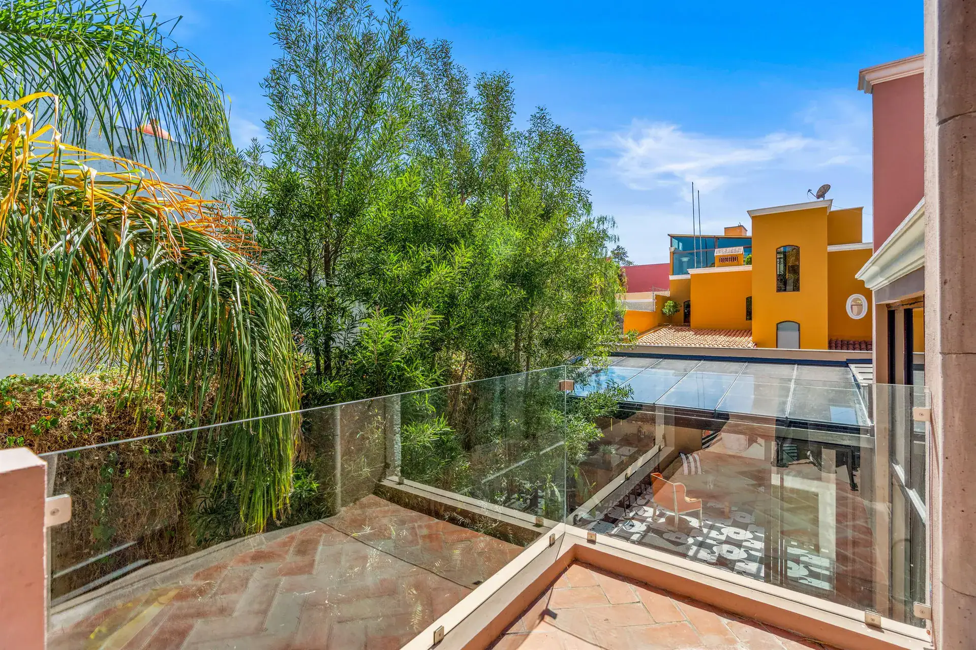 Villa Pacifica, terrace with a glass railing overlooking the garden and the neighboring yellow house, San Miguel de Allende
