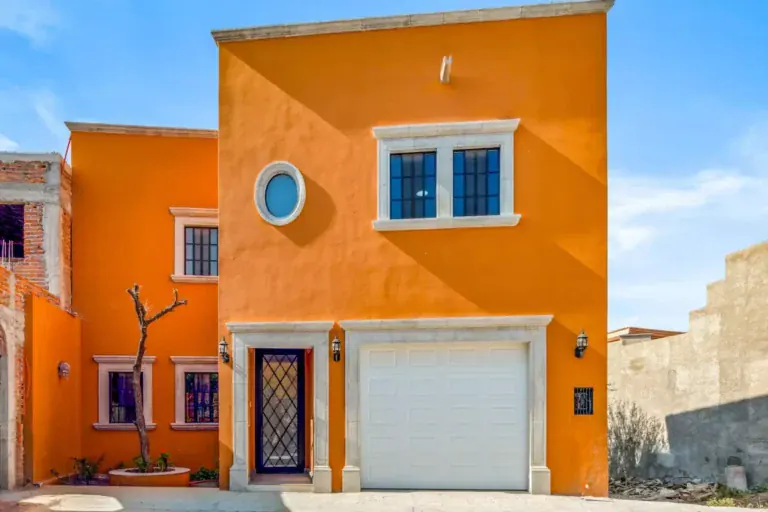 Villa Picasso, orange two-story house with a round window, stone-trimmed windows and a white garage door, San Miguel de Allende
