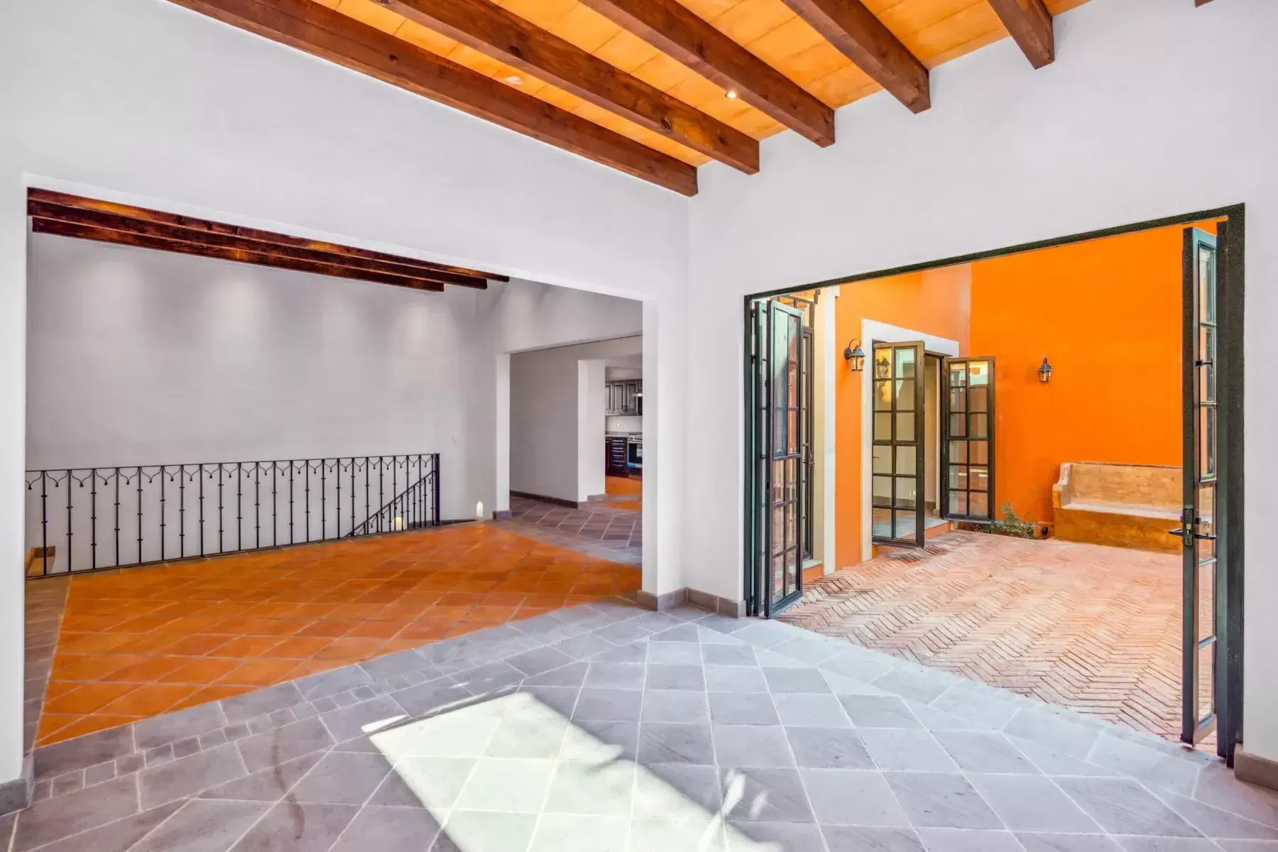 Villa Picasso, empty living space with a wood beam ceiling, a wrought iron balustrade and an open glass wall to the courtyard, San Miguel de Allende