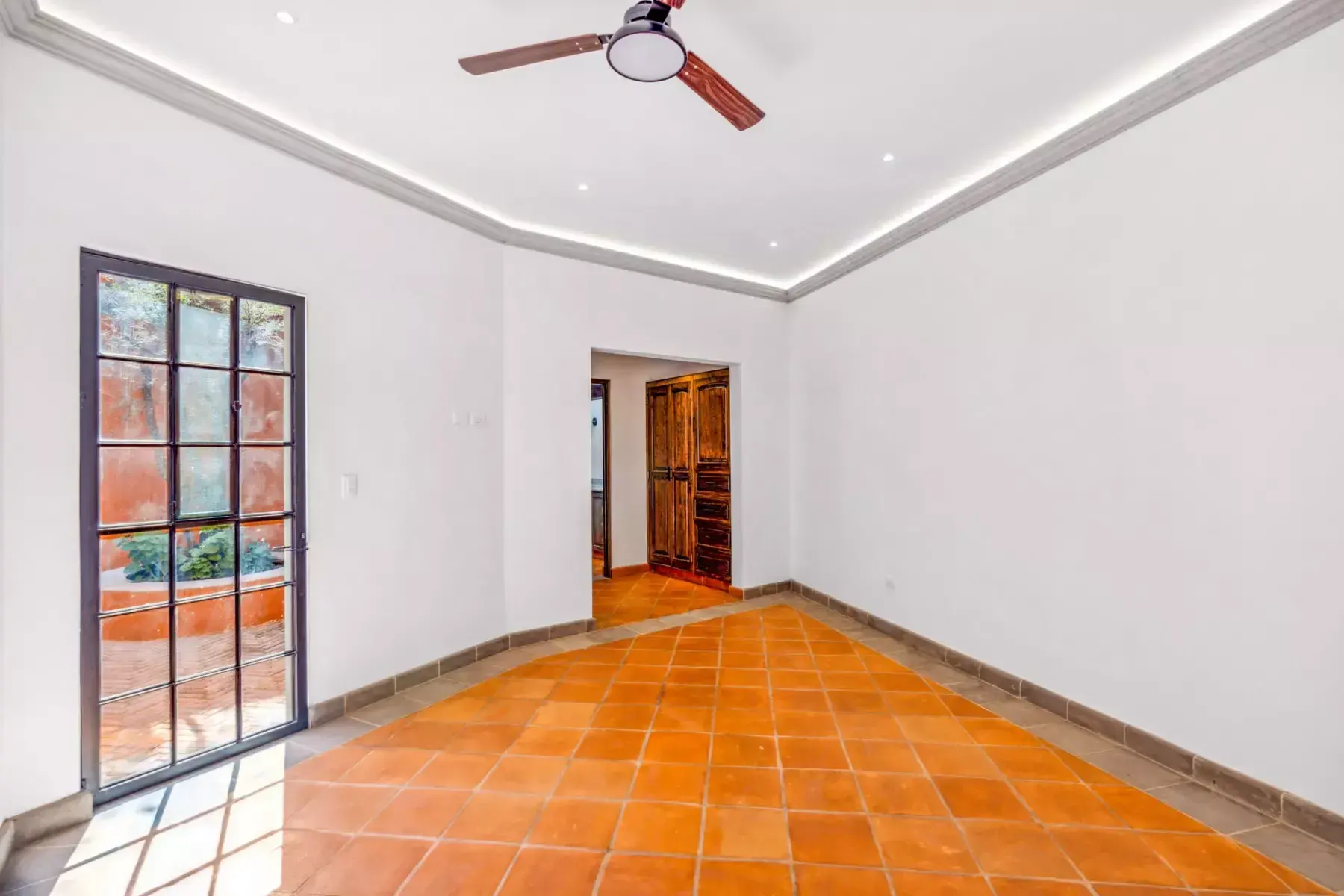 Villa Picasso, empty room with a ceiling fan, a glass door to a courtyard and a wood door at the end, San Miguel de Allende