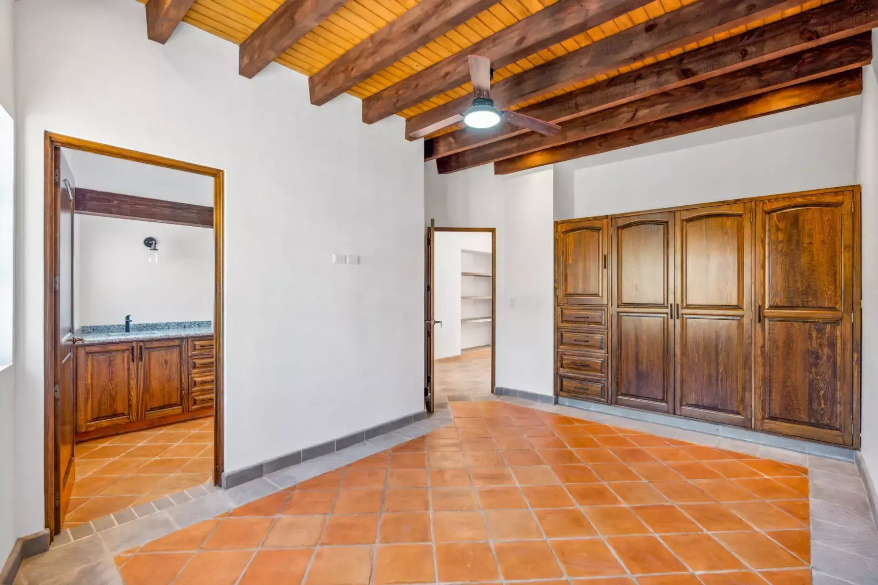 Villa Picasso, empty bedroom with a wood beam ceiling, built-in wooden wardrobes and a bathroom beyond, San Miguel de Allende