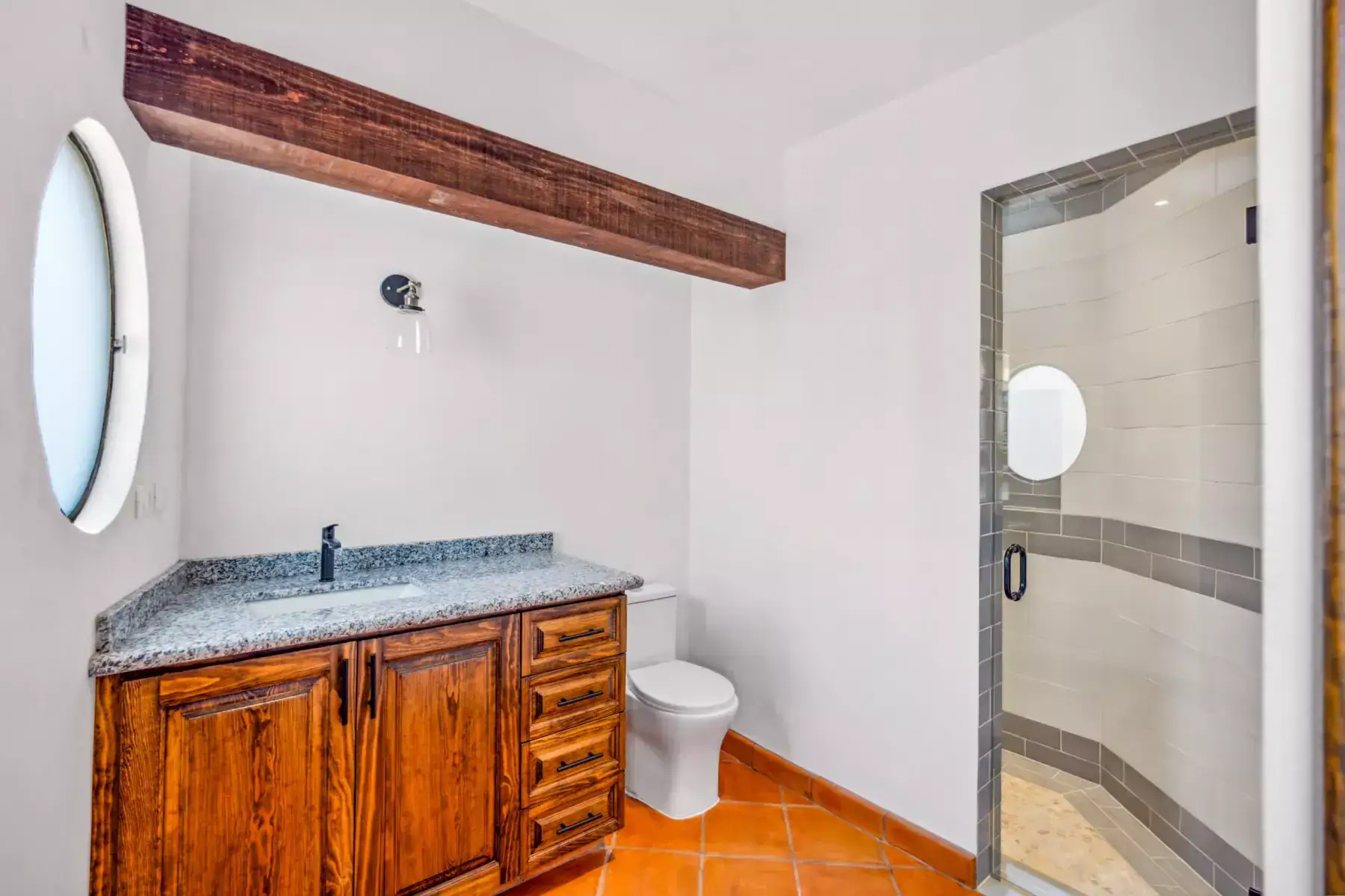 Villa Picasso, bathroom with a round window, a granite wood vanity and a glass shower, San Miguel de Allende