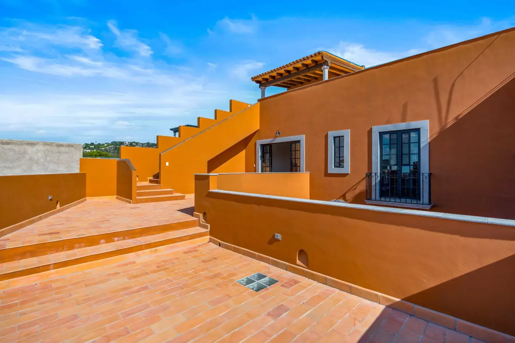 Villa Picasso, rooftop terrace with a herringbone brick floor, stairs and an orange parapet wall, San Miguel de Allende