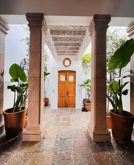 Symmetrical courtyard entry with two stone columns, a wooden door, and large potted tropical plants, San Miguel de Allende